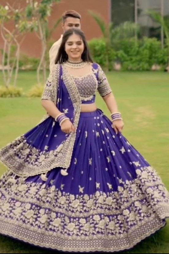 Woman in a traditional blue and white outfit standing outdoors with a blurred background
